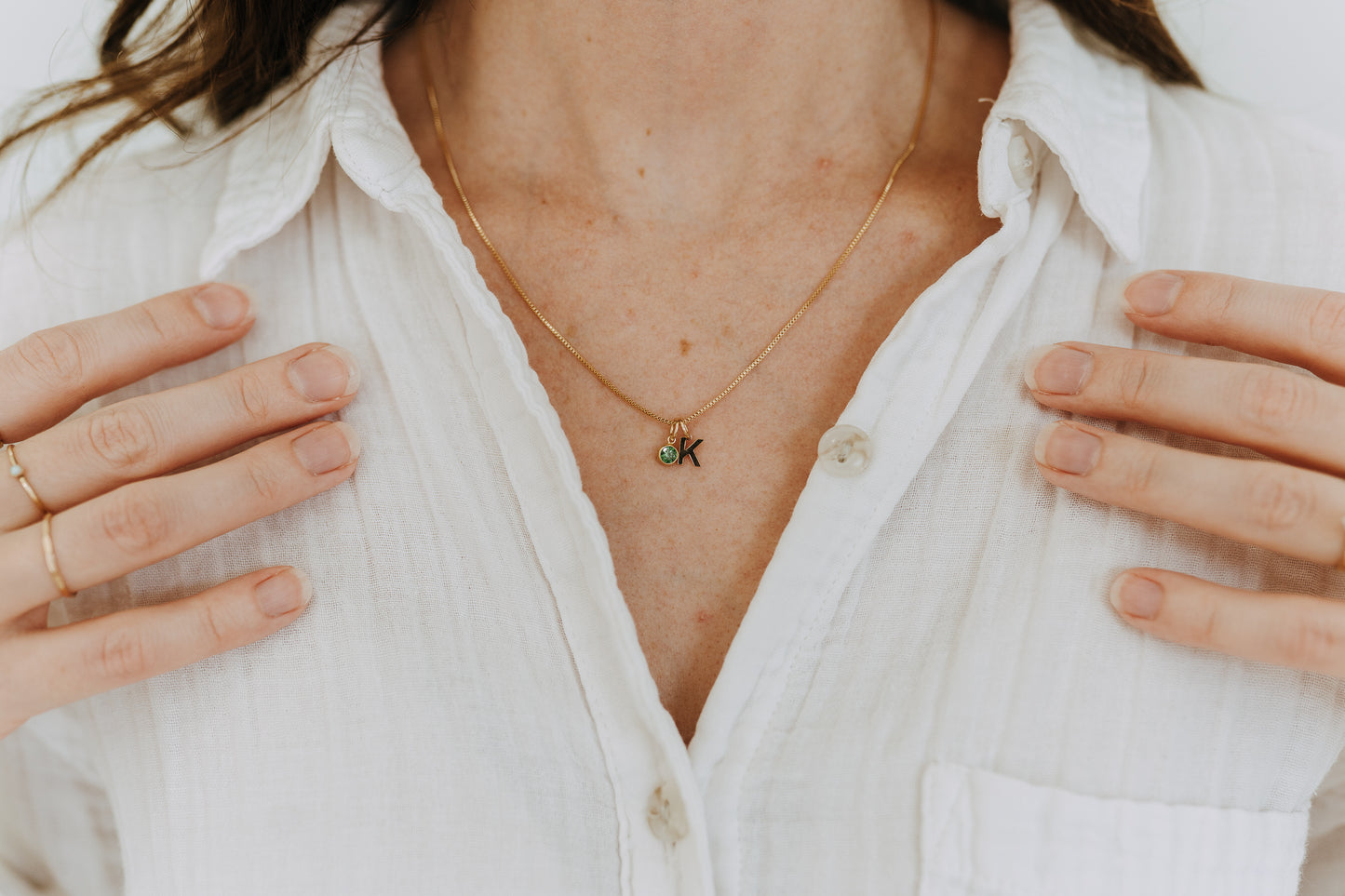Woman wearing gold filled initial and birthstone necklace layered with white blouse