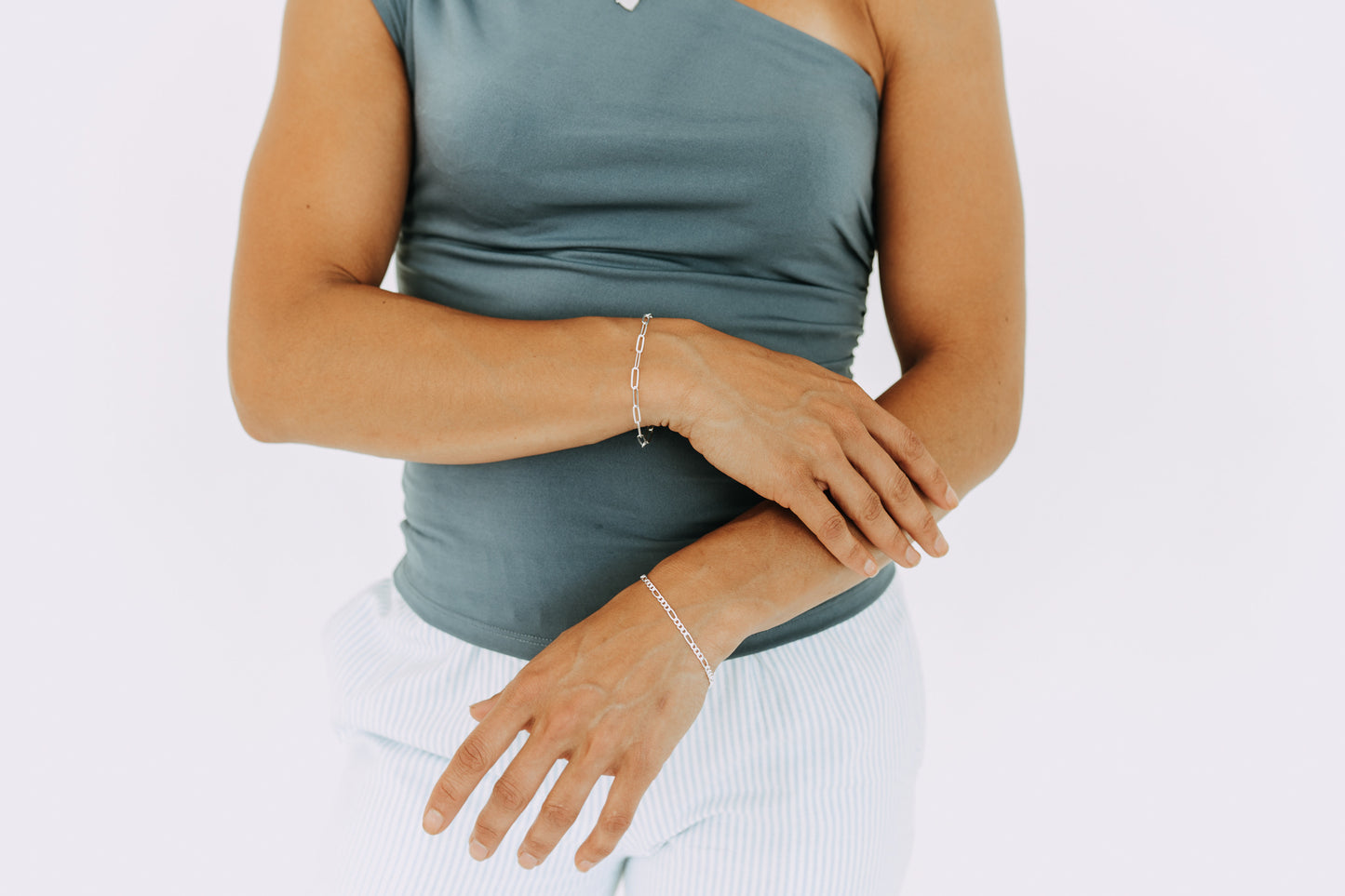 Woman wearing a 3mm sterling silver Figaro bracelet on wrist with matching silver jewelry