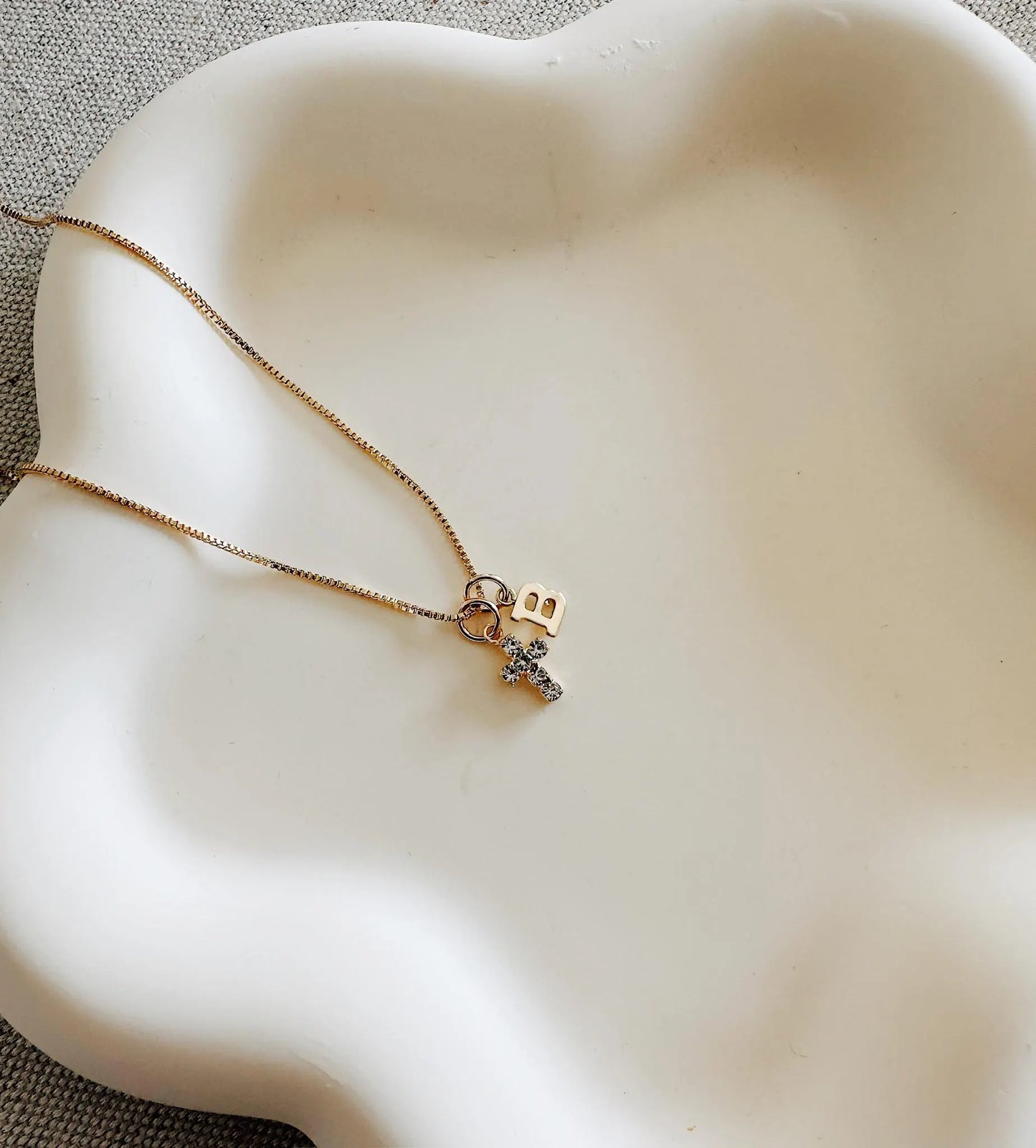 Gold cross necklace with birthstone and initial charm layered on a delicate chain