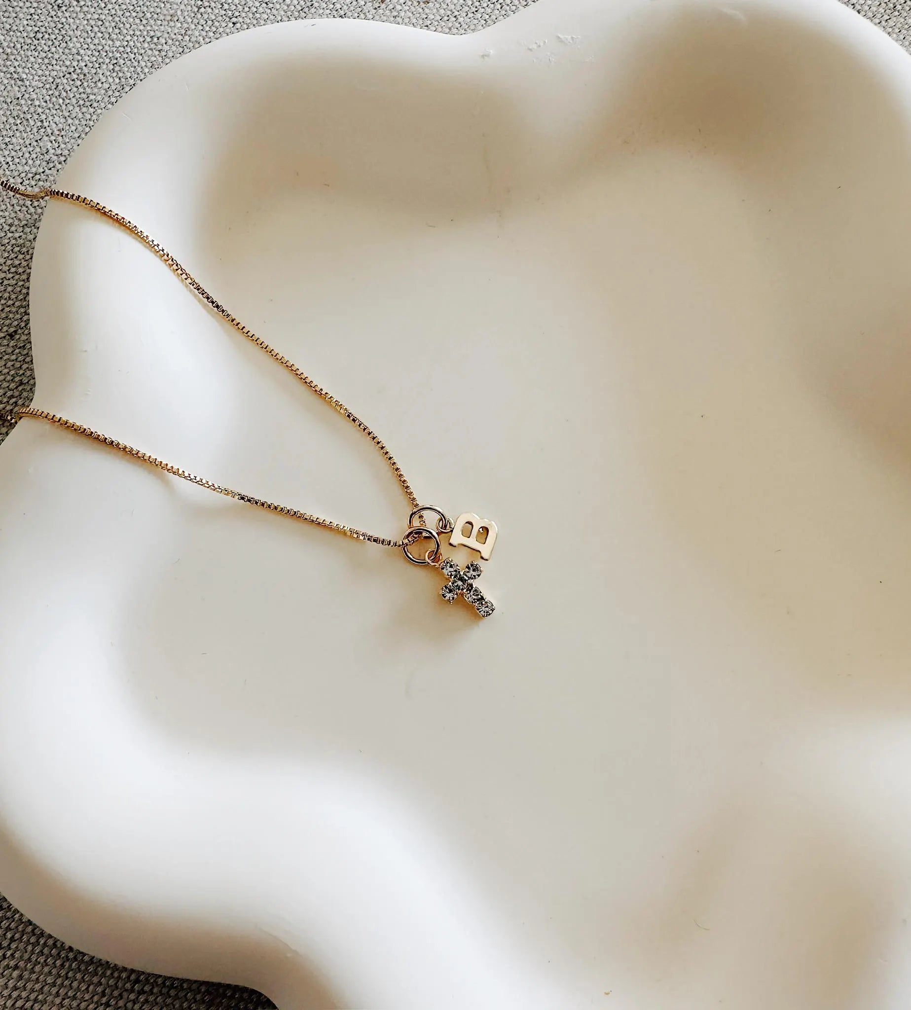 Gold cross necklace with birthstone and initial charm layered on a delicate chain
