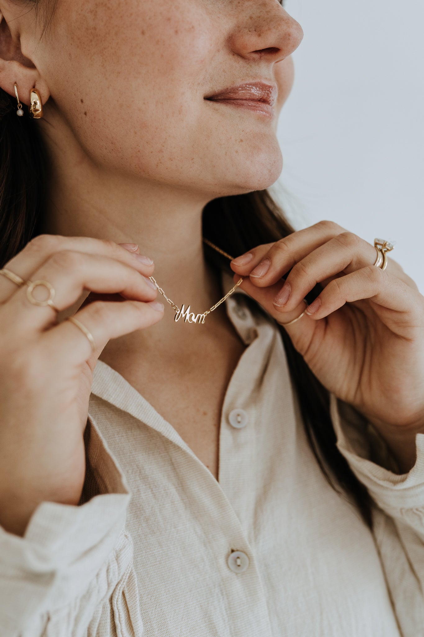 Minimalist gold Mom necklace worn at the collarbone with a lightweight cream linen blouse.