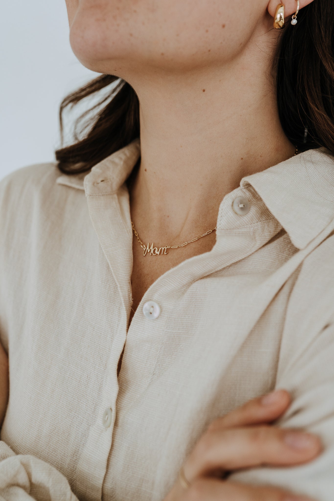 Gold filled Mom necklace layered with other gold necklaces on a woman wearing a cream button-up shirt.