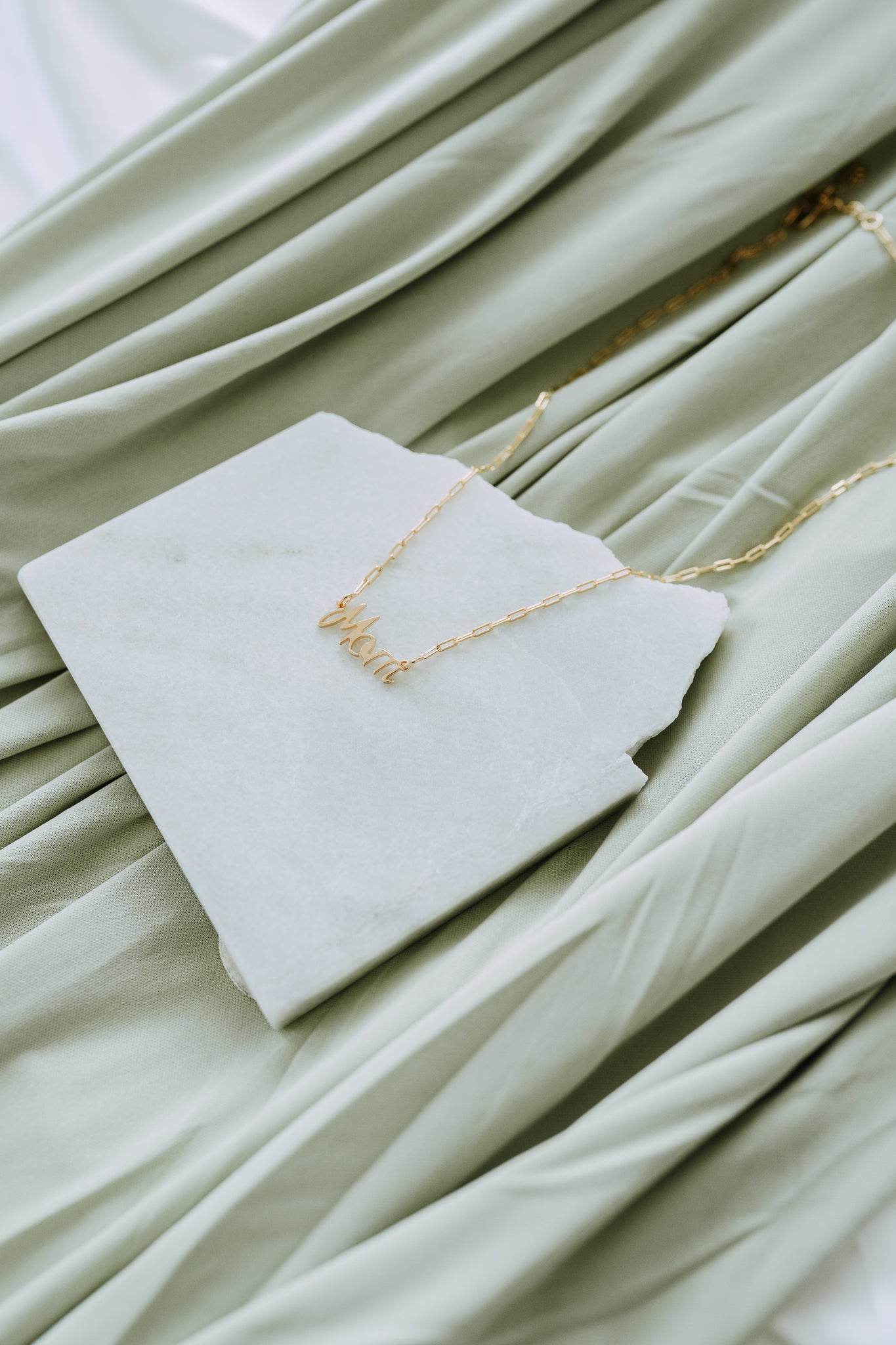 Close-up of gold Mom pendant necklace featuring elegant cursive lettering.