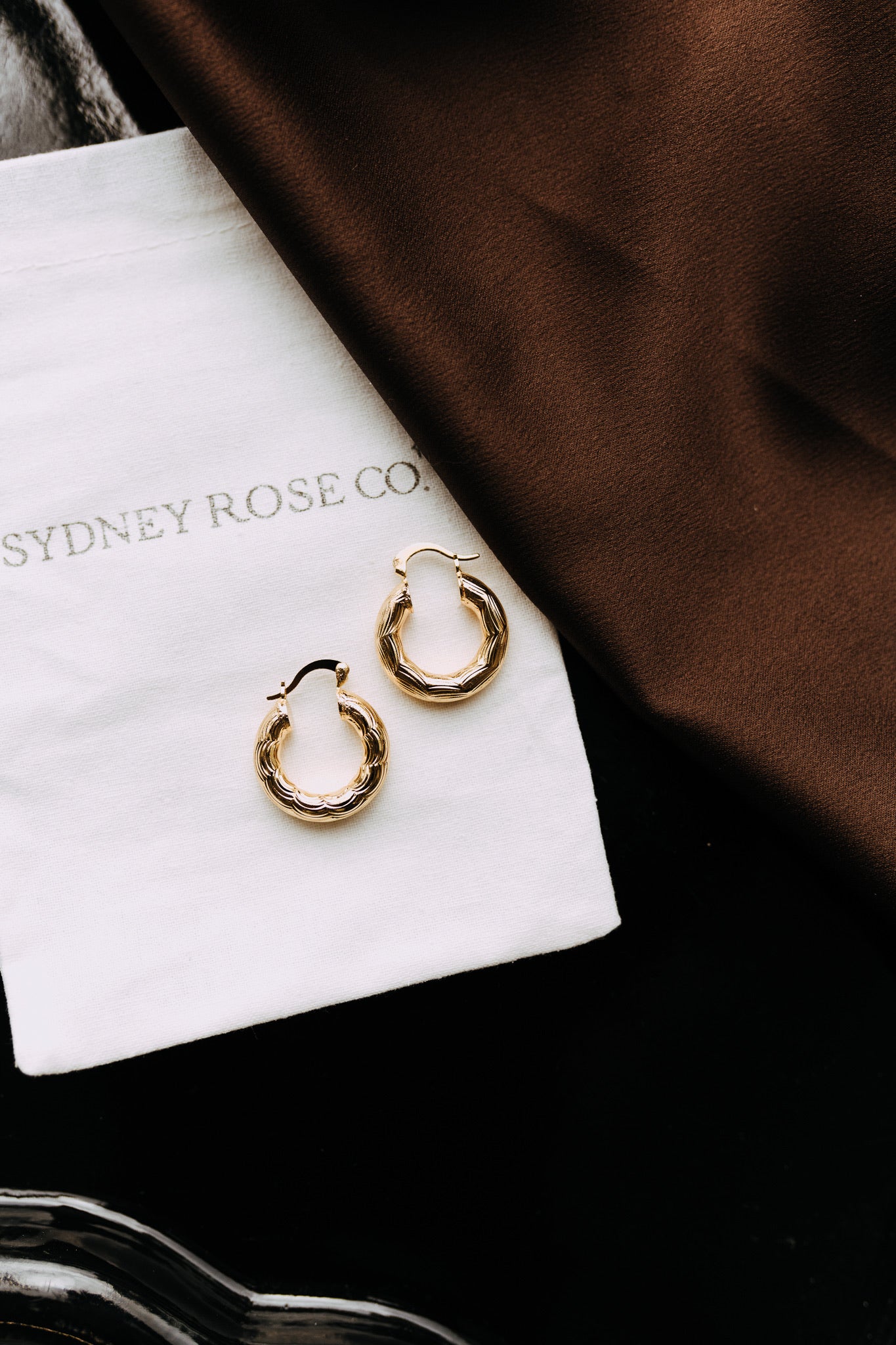 Gold filled Camellia hoops styled flat lay on Sydney Rose Co. pouch