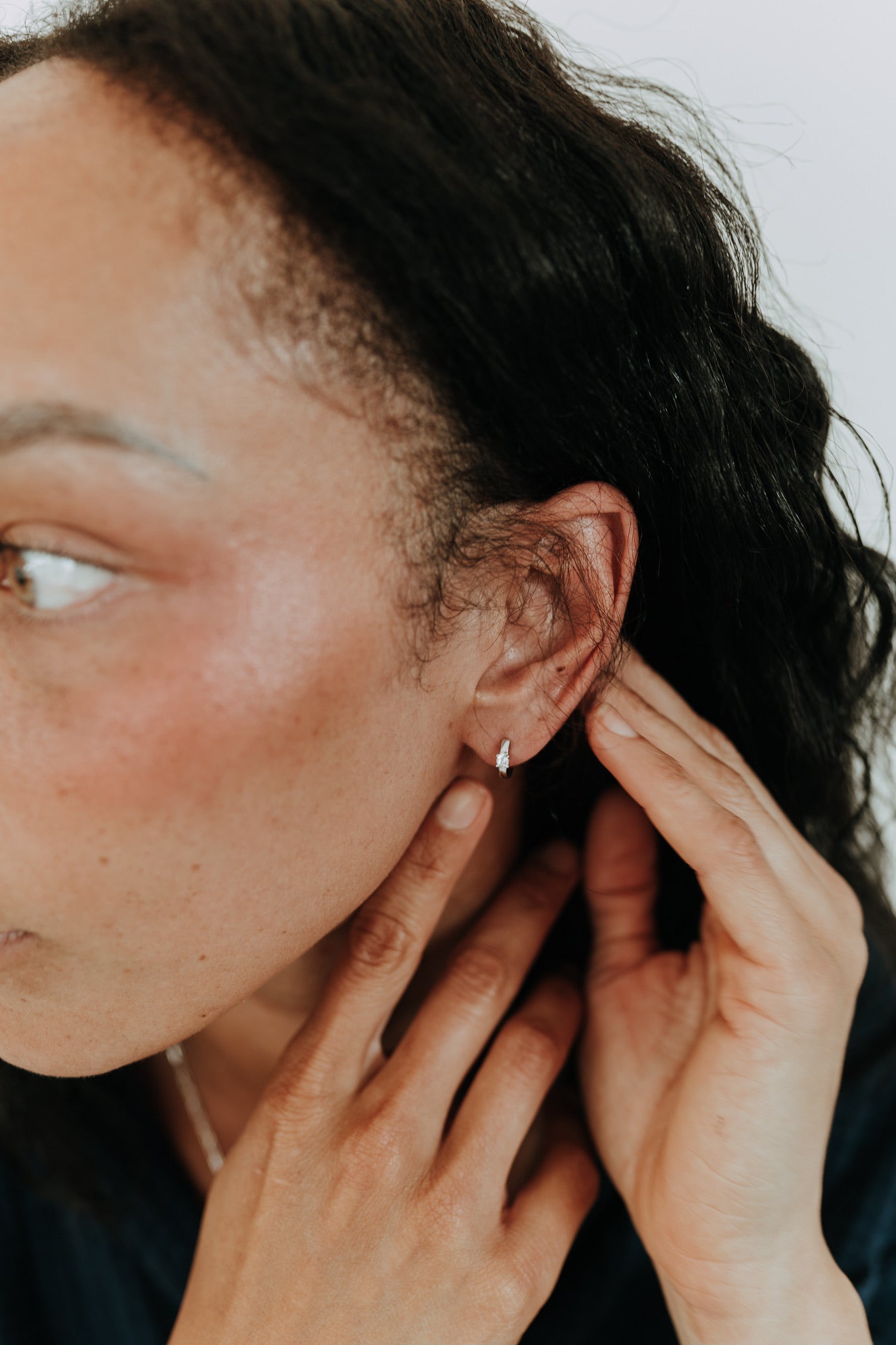 Model wearing Twilight sterling silver CZ huggie hoops with sparkling cubic zirconia stones.