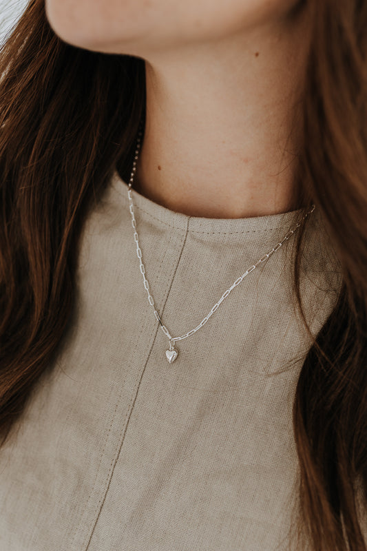 Close-up of a sterling silver heart charm necklace featuring a modern paperclip chain