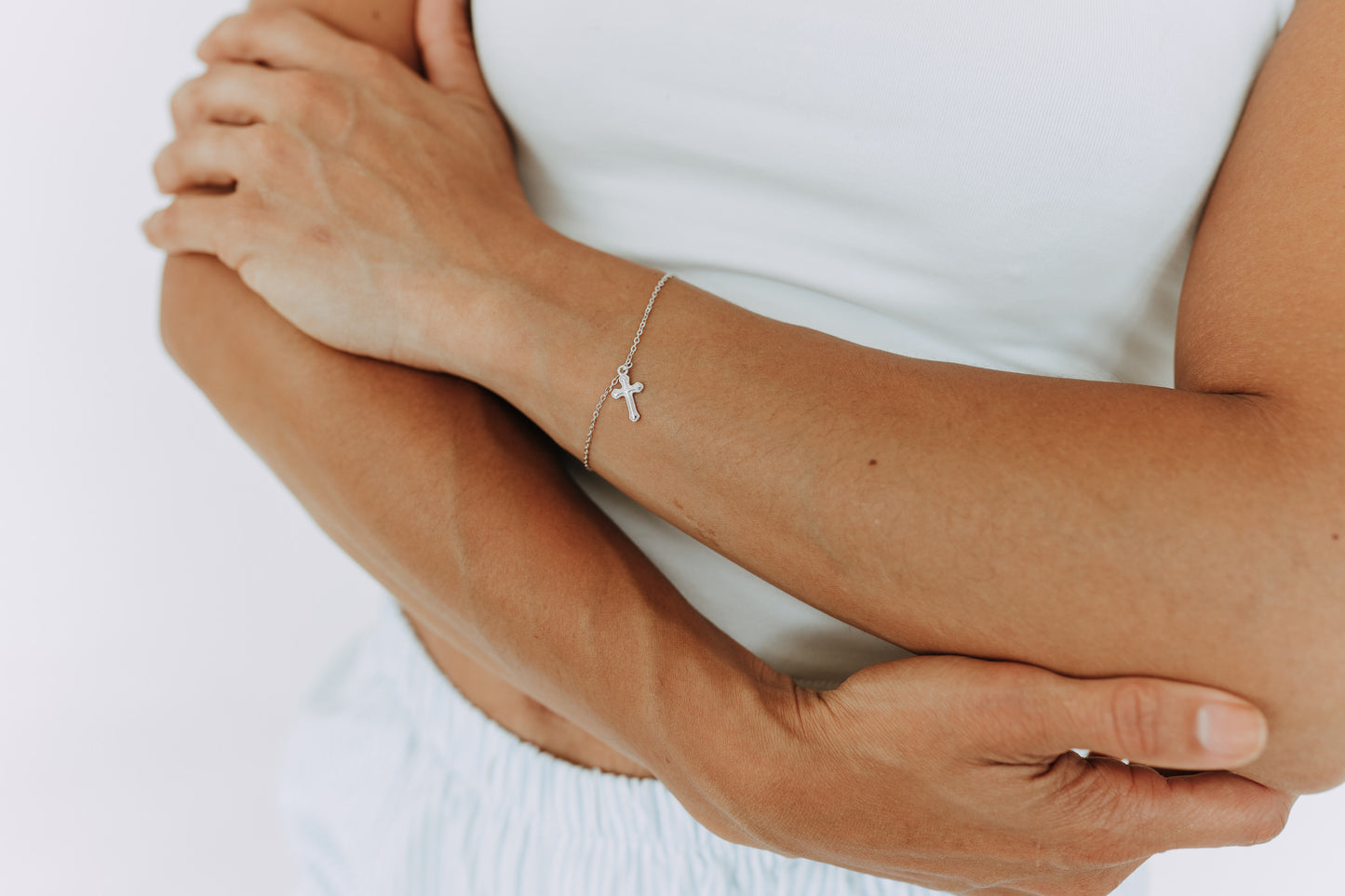 Dainty sterling silver cross charm bracelet worn on woman's wrist.