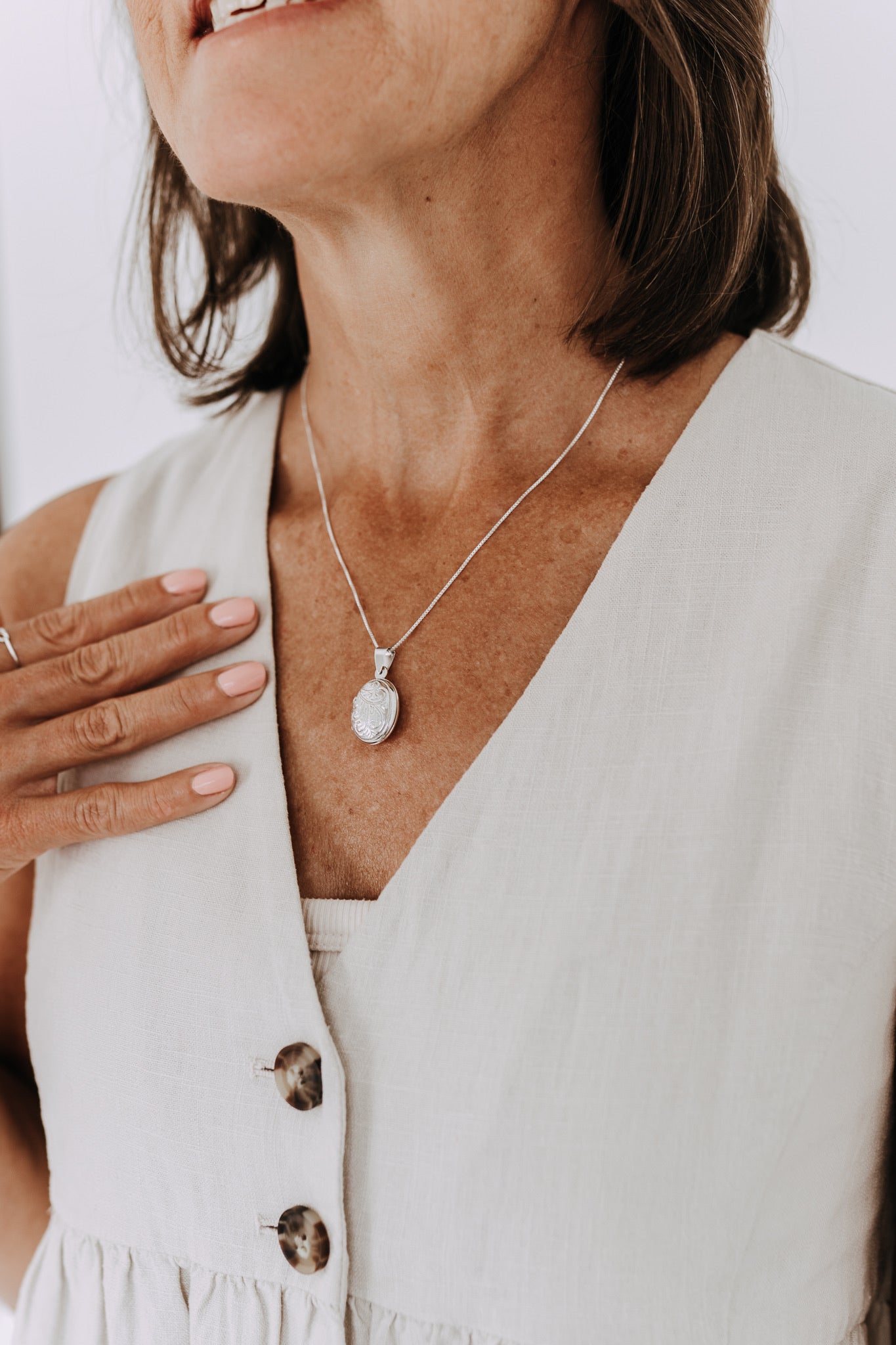 Sterling silver oval engraved locket necklace on a delicate box chain worn with a neutral linen top.
