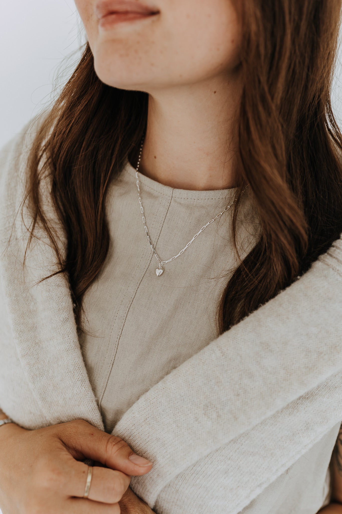 Model wearing a sterling silver heart pendant necklace styled with a neutral linen top