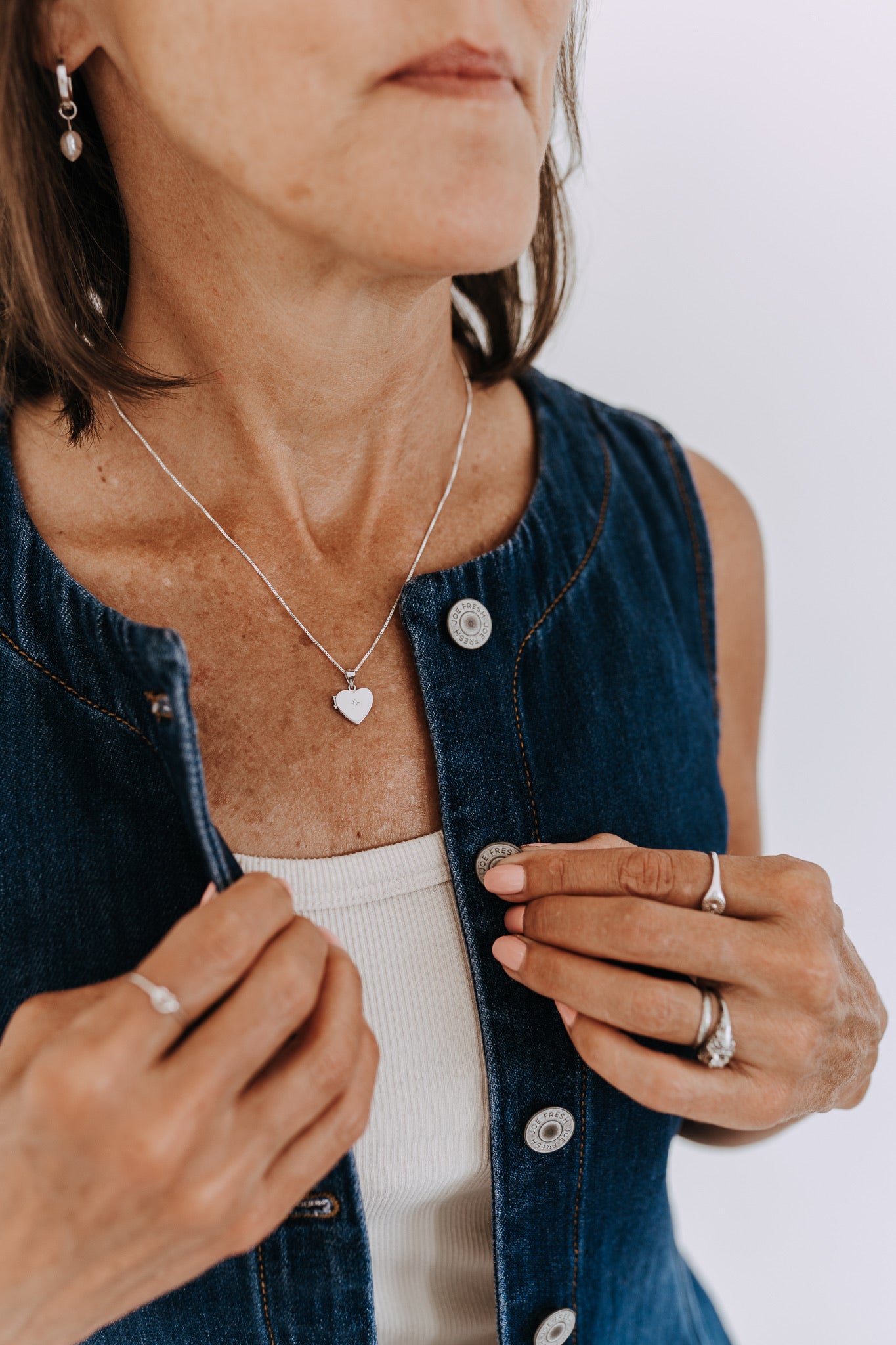 Sterling silver heart locket necklace with cubic zirconia worn on a denim vest.