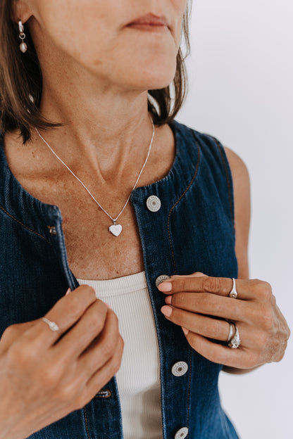Sterling silver heart locket necklace with cubic zirconia worn on a denim vest.