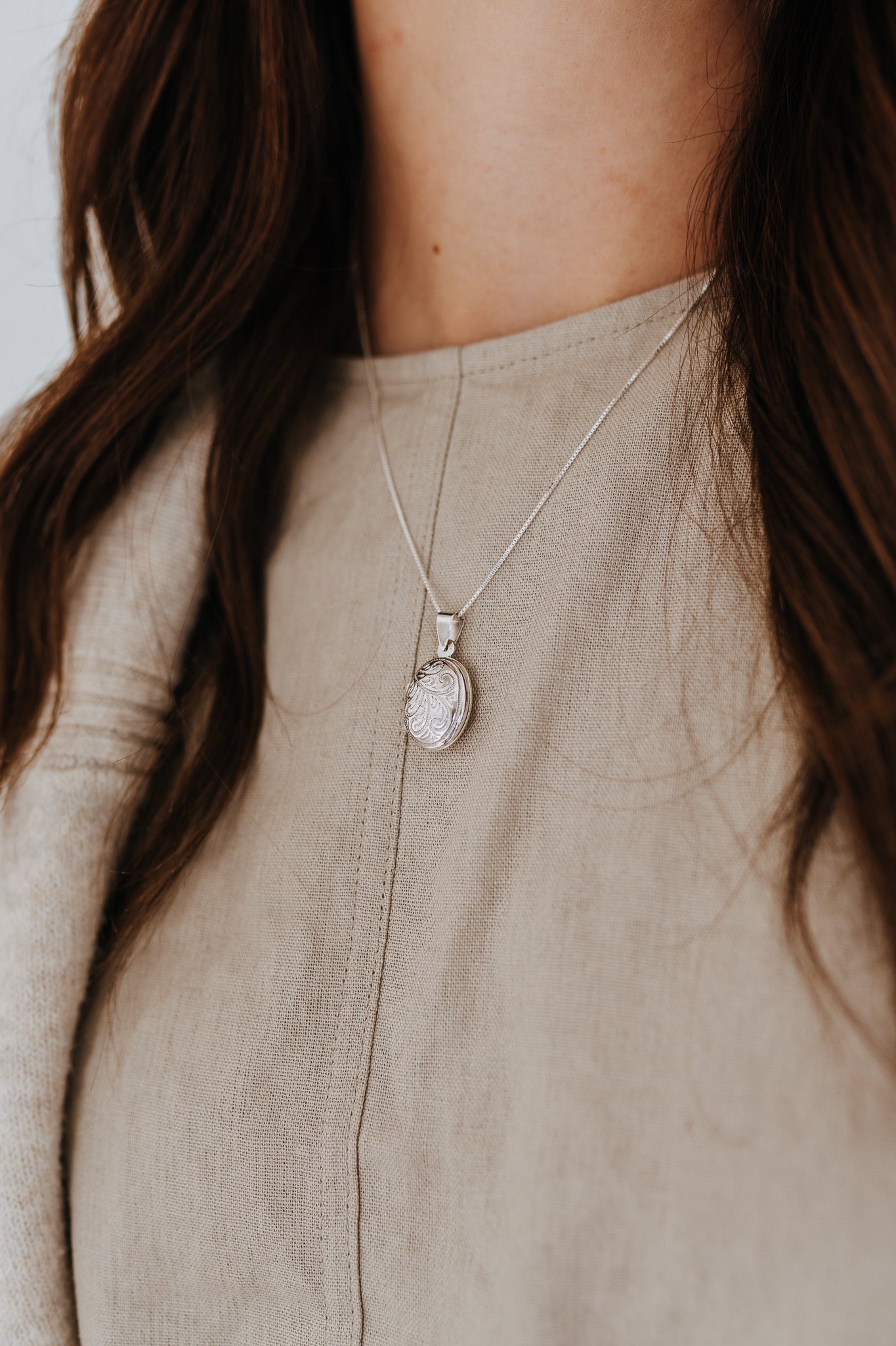 Close-up of sterling silver oval locket necklace featuring an engraved heirloom-inspired design.