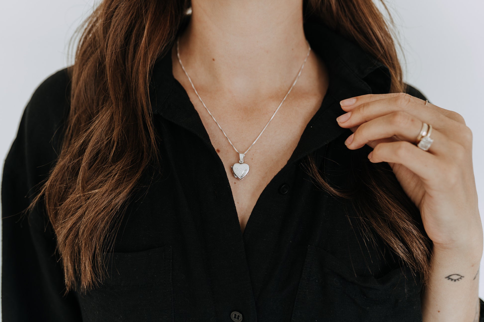 Close-up of engraved sterling silver heart locket on a delicate box chain.