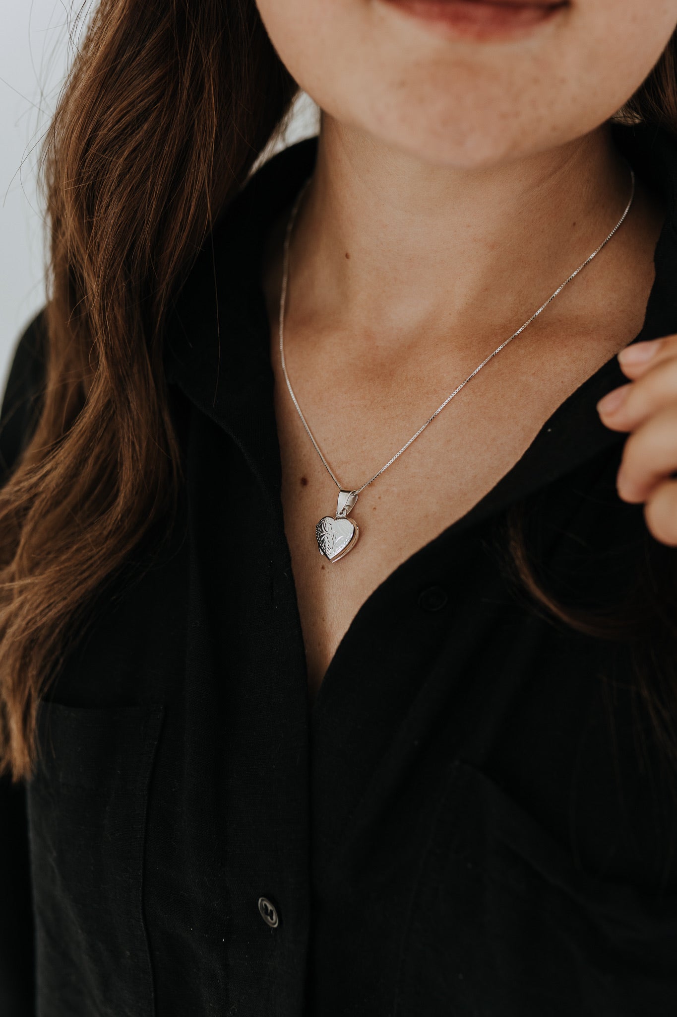 Woman wearing a sterling silver heart locket necklace with engraved heart detail.
