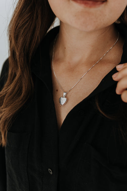 Woman wearing a sterling silver heart locket necklace with engraved heart detail.