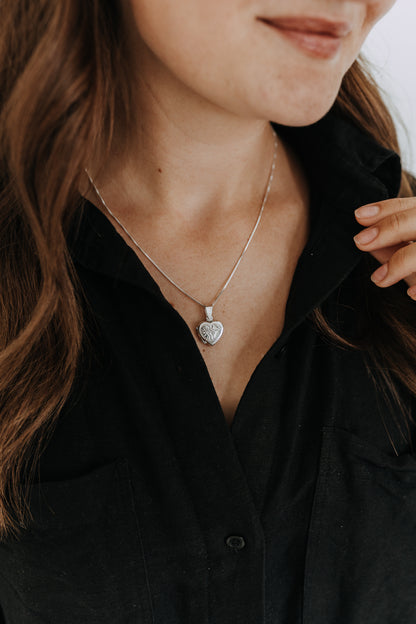 Delicate sterling silver heart locket necklace worn with a black button-up shirt.