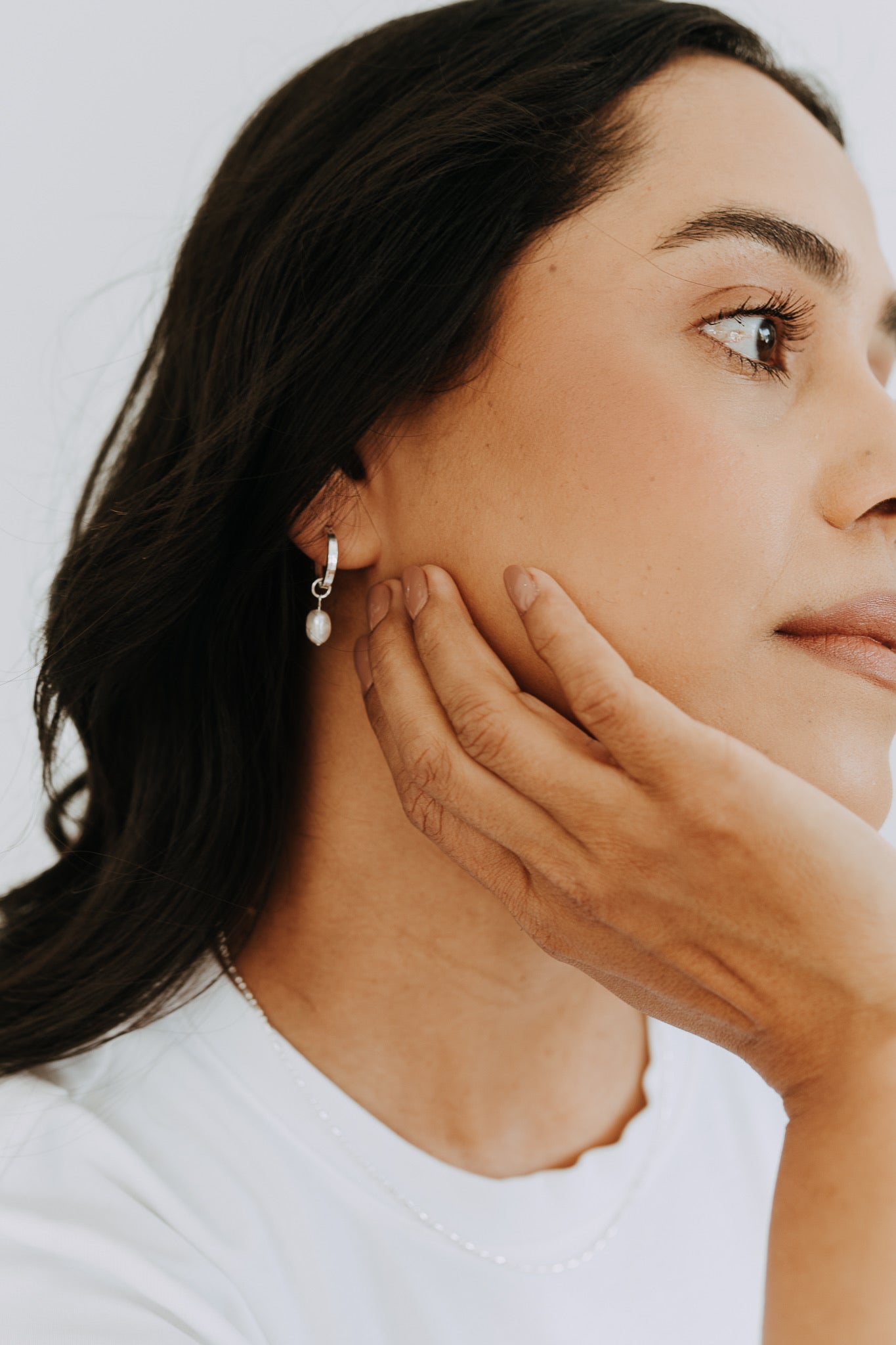 Close-up of sterling silver huggie hoop earrings featuring removable freshwater pearl drops.