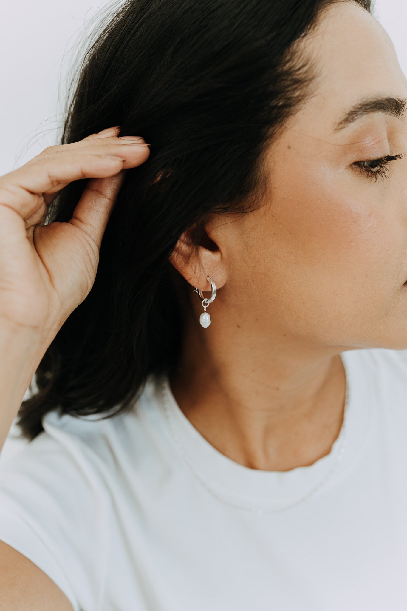 Side profile of model wearing sterling silver hoop earrings with dangling freshwater pearls.