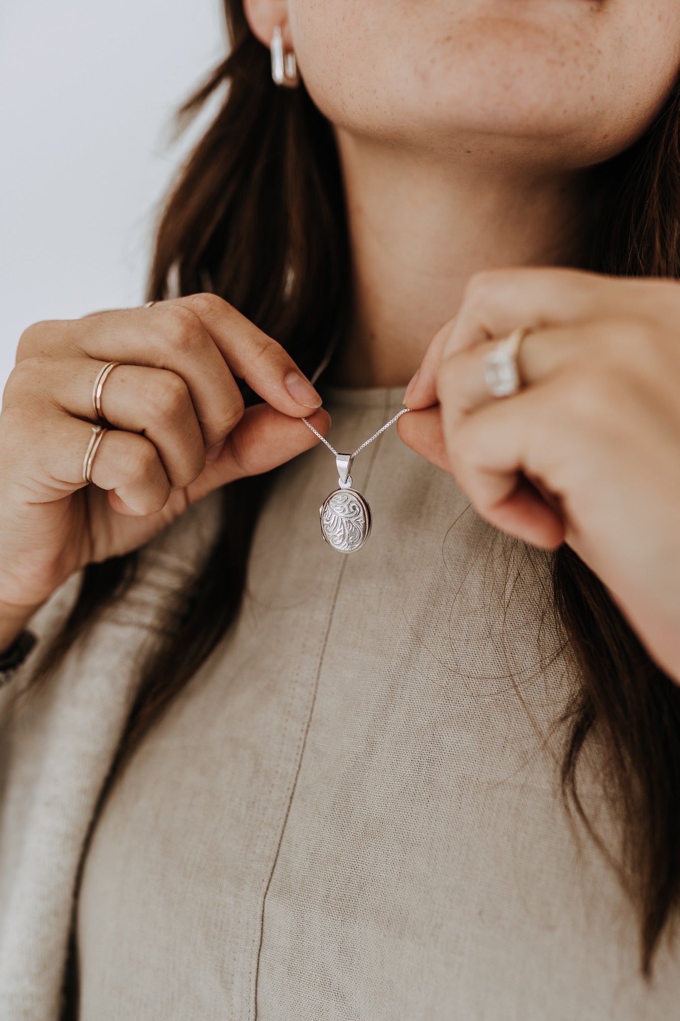 Model holding sterling silver oval locket necklace to showcase the engraved pendant.