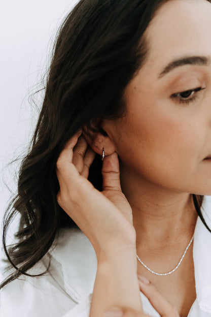 Sterling silver 15mm huggie hoop earrings with tiny cubic zirconia stone worn by model.