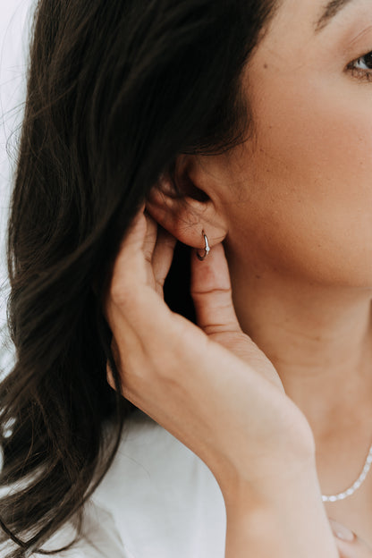 Model wearing Bay sterling silver huggie hoops featuring a single cubic zirconia stone accent.