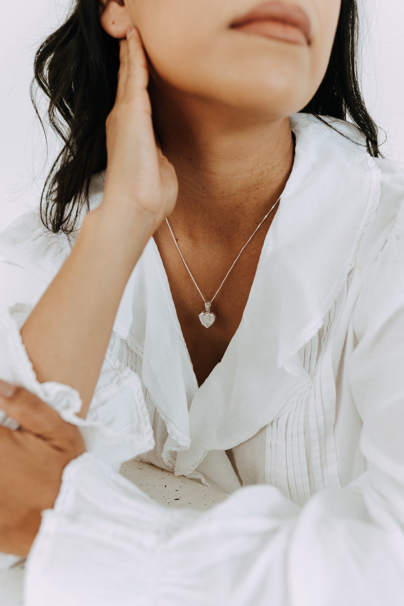 Woman wearing a sterling silver heart locket necklace with engraved heart detail.