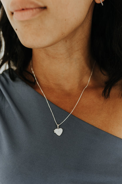 Woman wearing sterling silver heart locket necklace on a blue one-shoulder top.