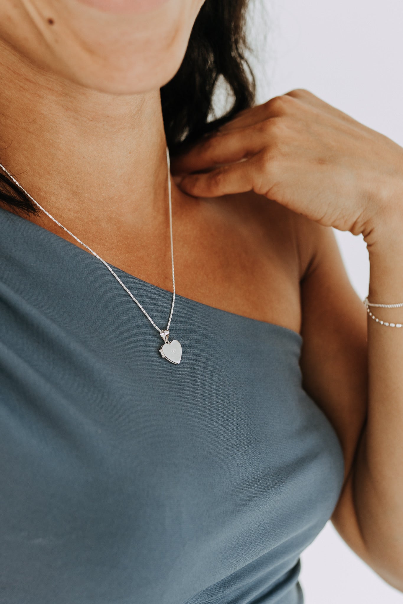 Woman wearing sterling silver heart locket necklace on a blue one-shoulder top.