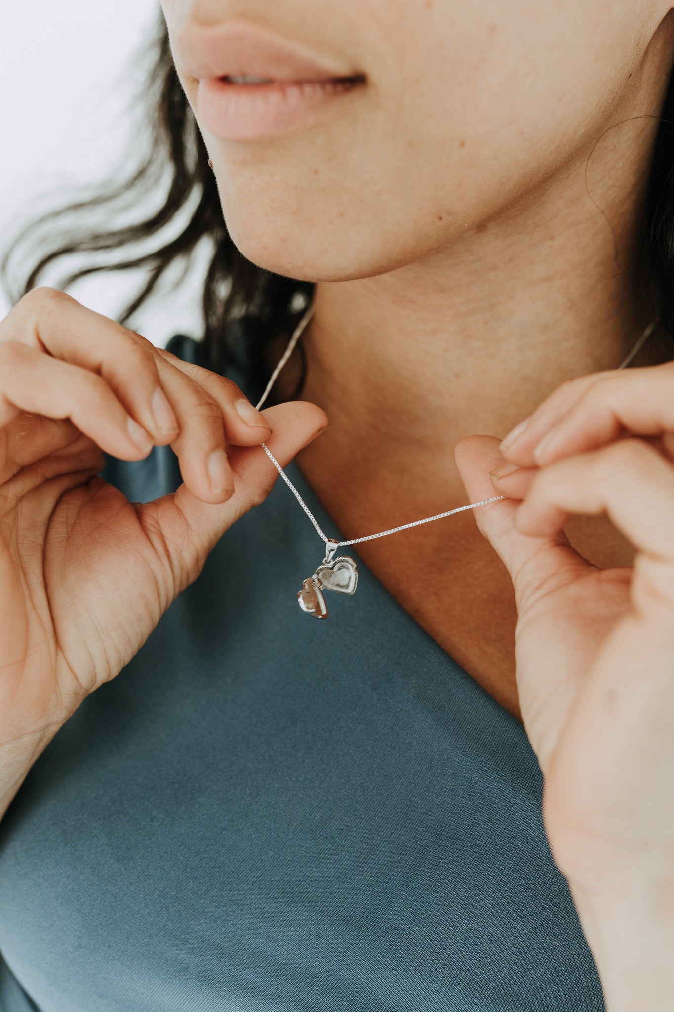 Open heart locket necklace in sterling silver held between hands.