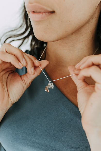 Open heart locket necklace in sterling silver held between hands.