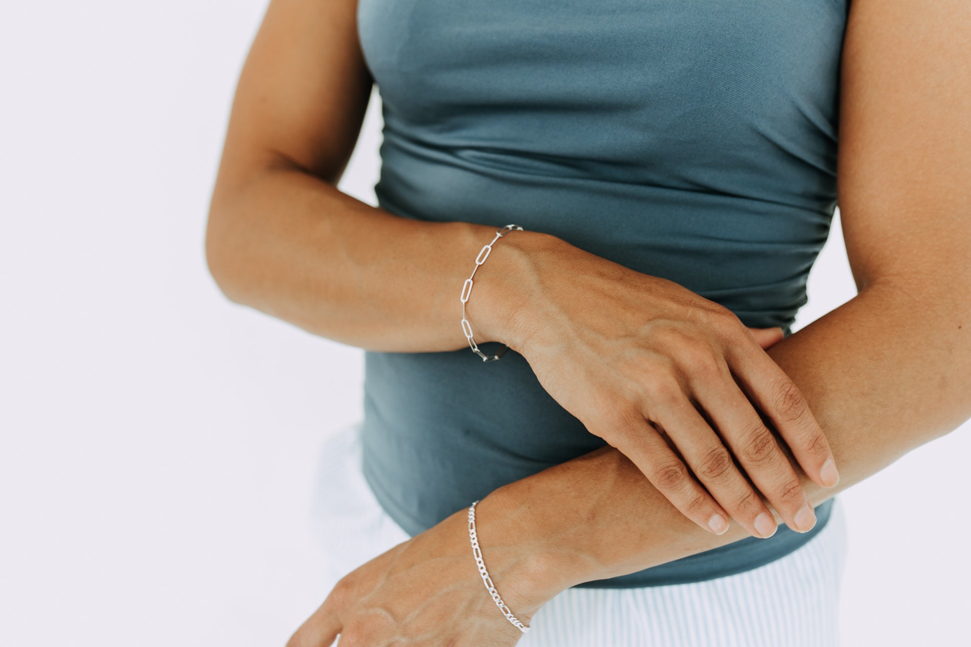 Woman wearing a 3mm sterling silver Figaro bracelet on wrist with matching silver jewelry.