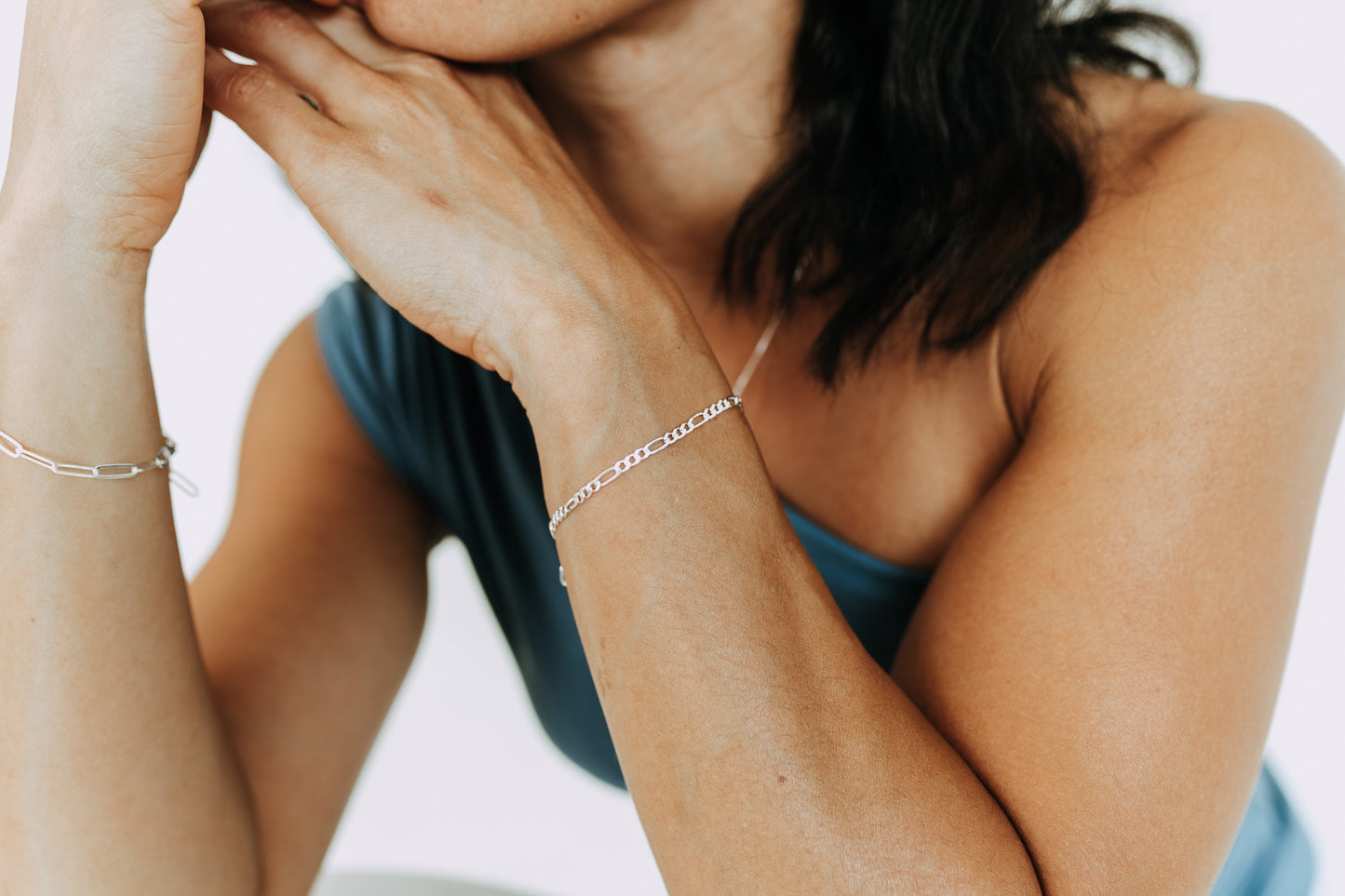 Woman wearing a 3mm sterling silver Figaro bracelet on wrist with matching silver jewelry.