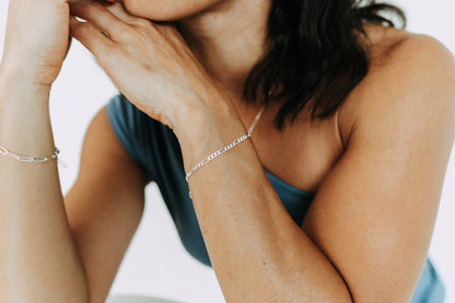 Woman wearing a 3mm sterling silver Figaro bracelet on wrist with matching silver jewelry.