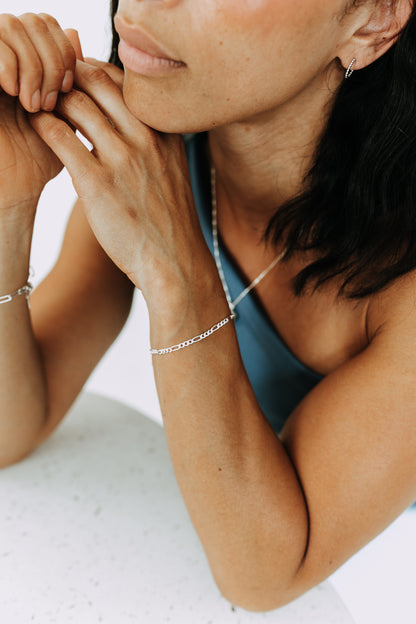 Close-up of sterling silver Figaro chain bracelet featuring classic alternating links.