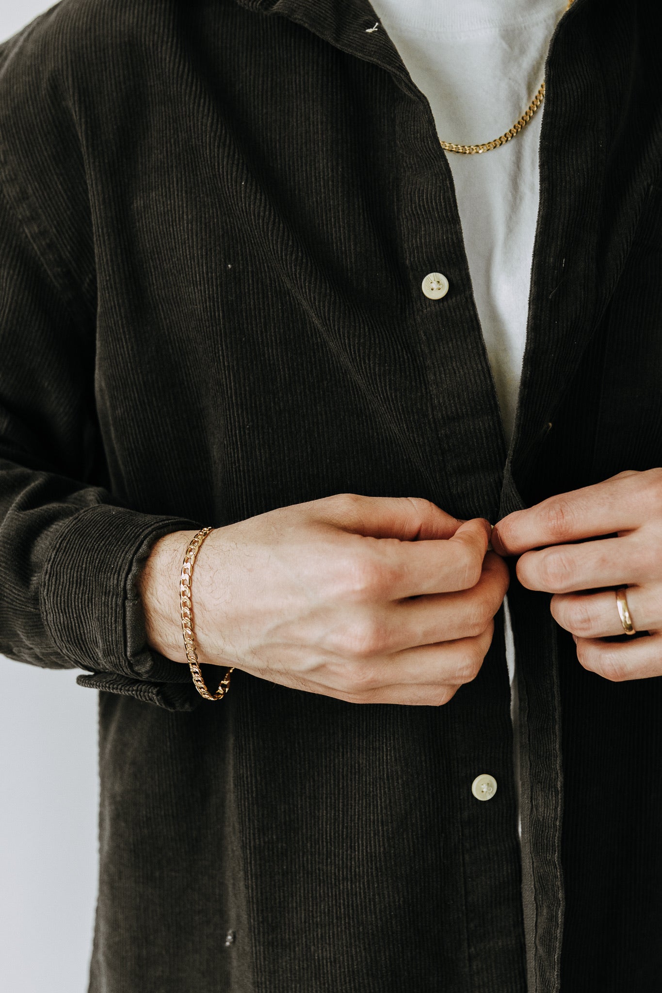Men’s gold chain bracelet paired with black corduroy overshirt and layered jewelry styling