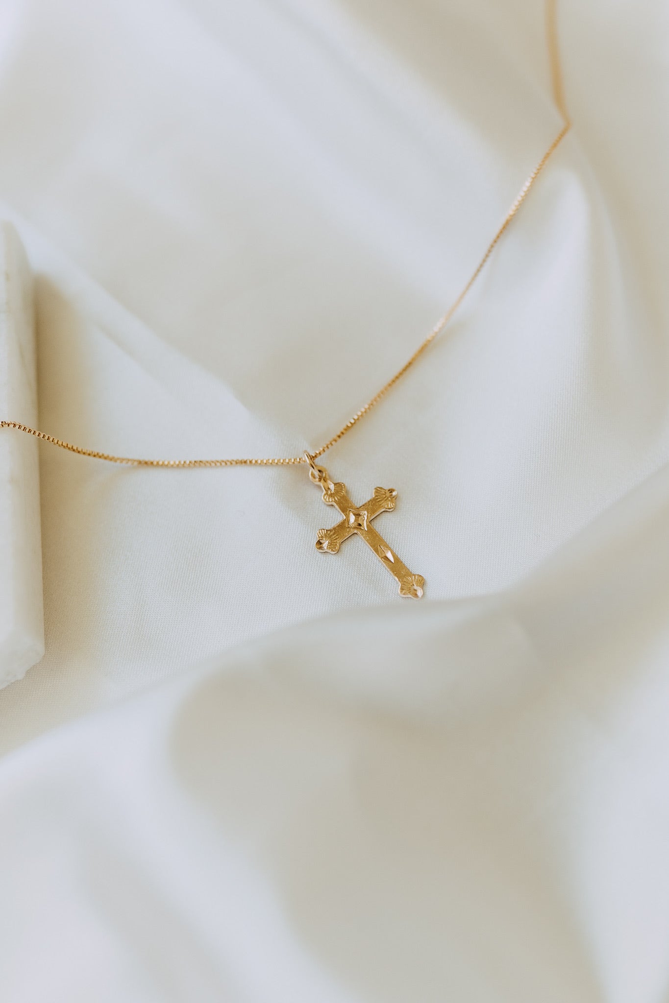 Gold cross necklace photographed on soft white fabric