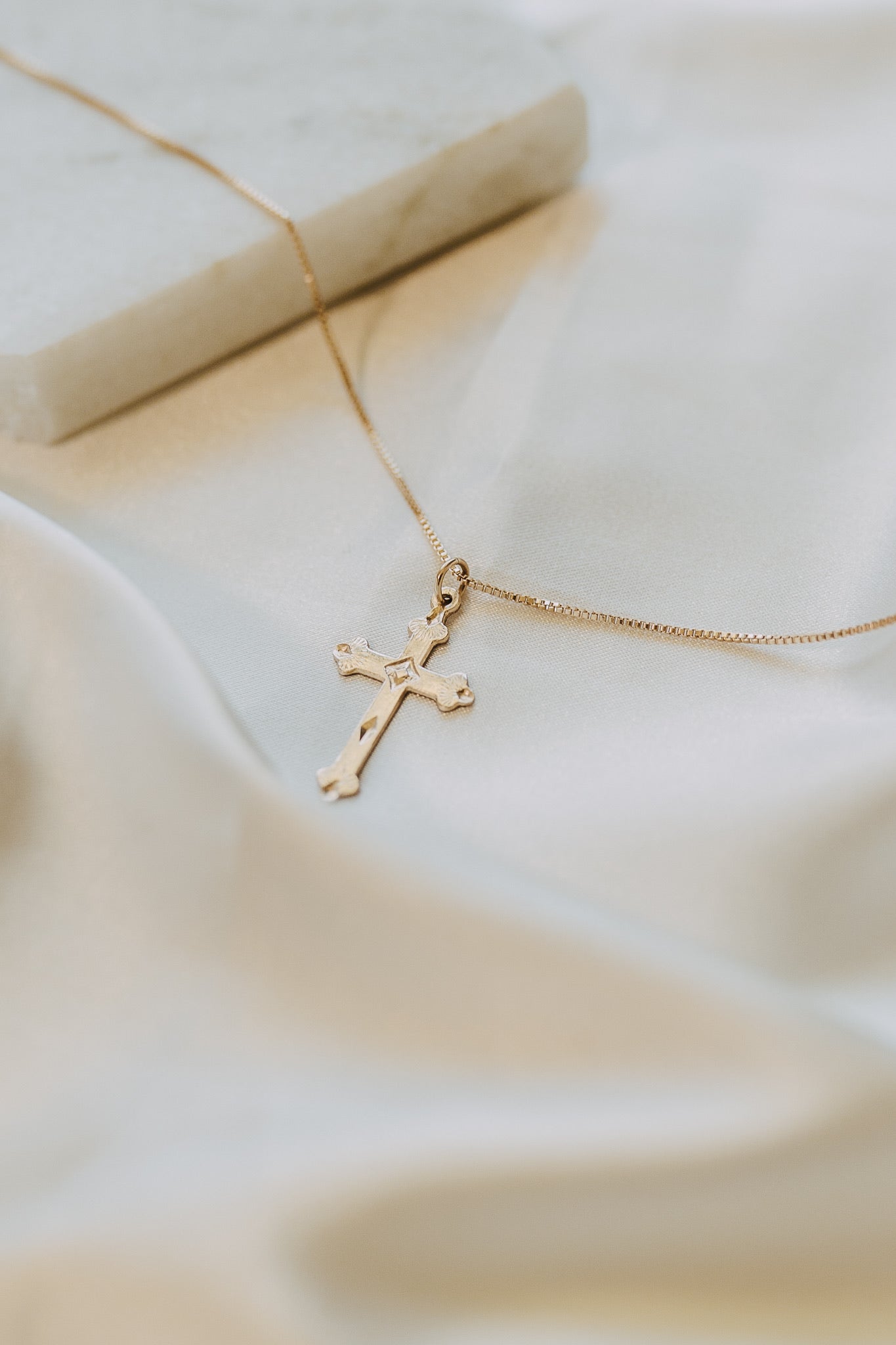 Gold cross necklace photographed on soft white fabric