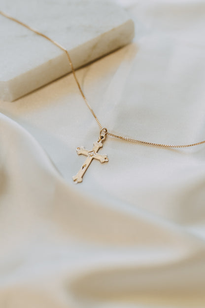 Gold cross necklace photographed on soft white fabric