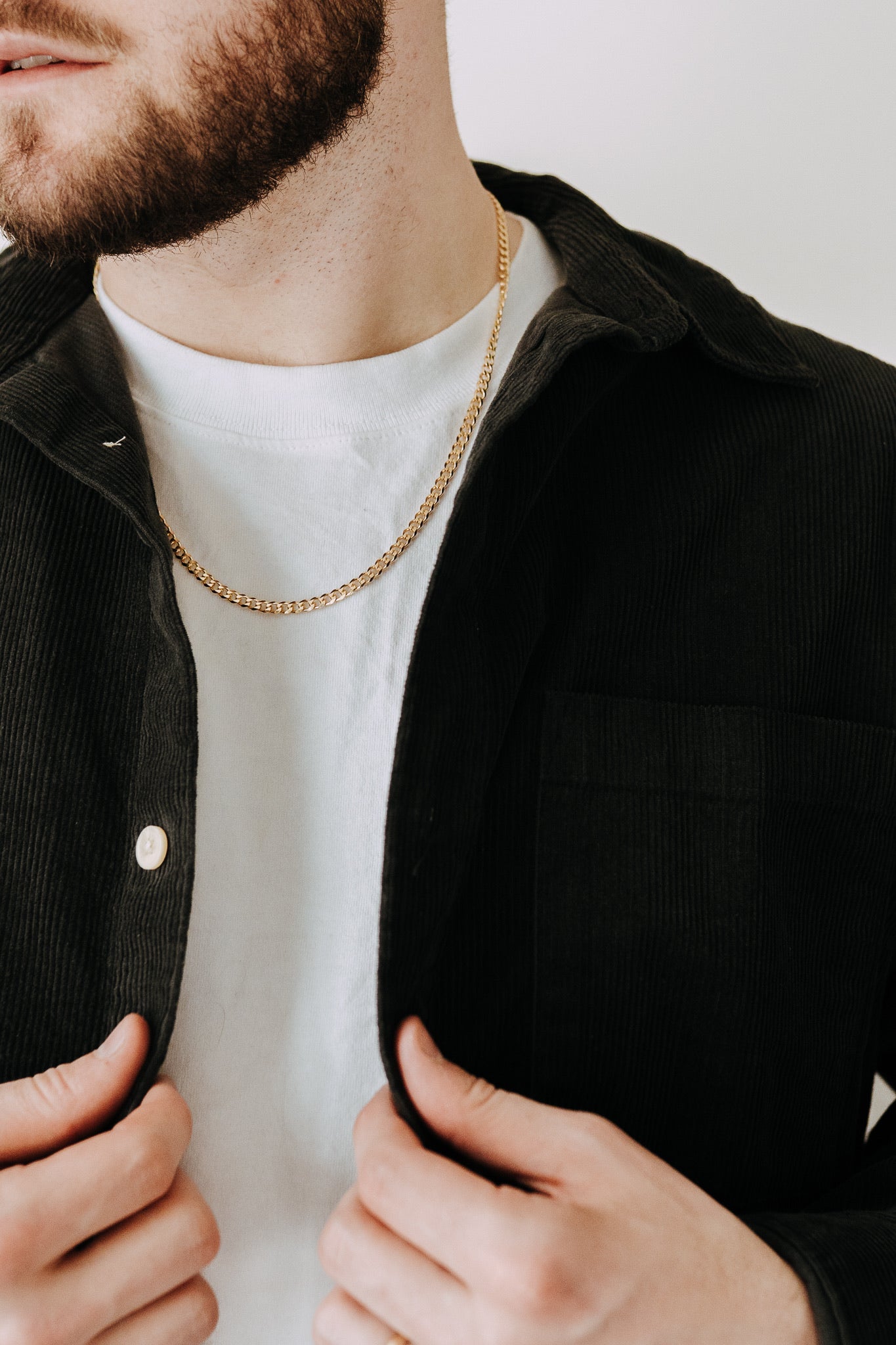 Men’s gold curb chain necklace layered with black corduroy overshirt and white tee