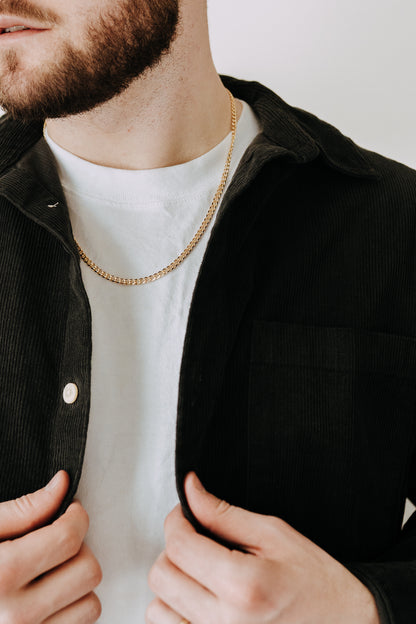 Men’s gold curb chain necklace layered with black corduroy overshirt and white tee