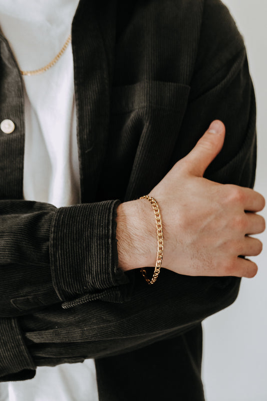 Men’s gold chain bracelet paired with black corduroy overshirt and layered jewelry styling