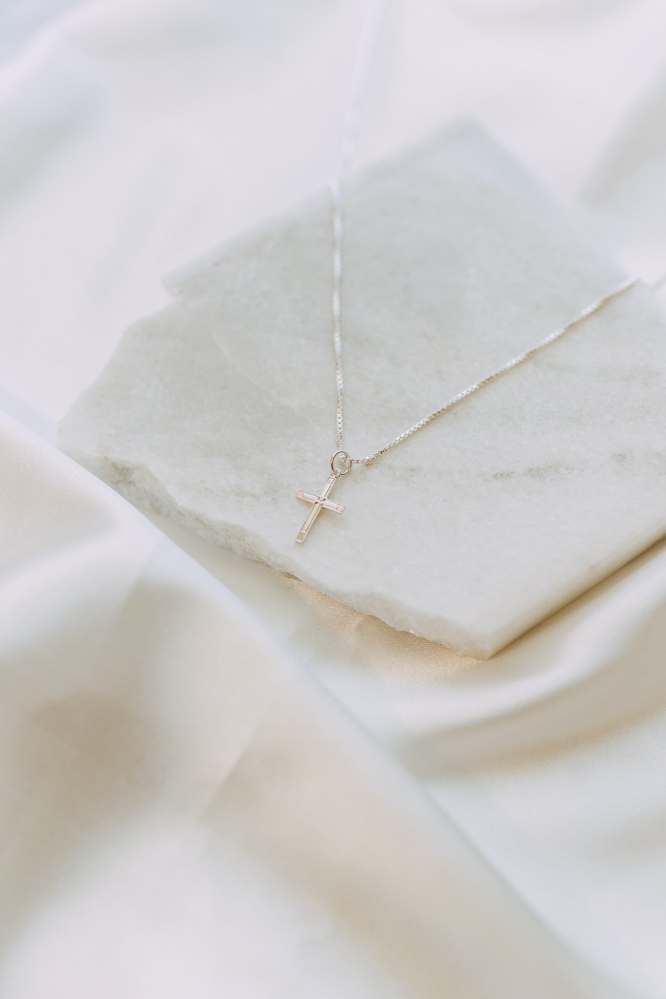 Sterling silver cross pendant necklace photographed on neutral stone tray