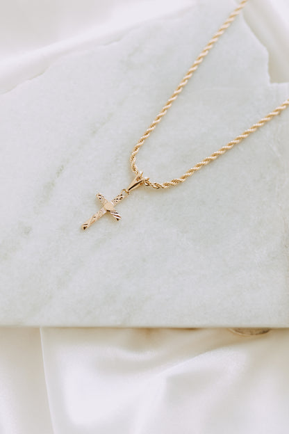 Flat lay of engraved gold cross pendant necklace on a twisted rope chain over white marble backdrop