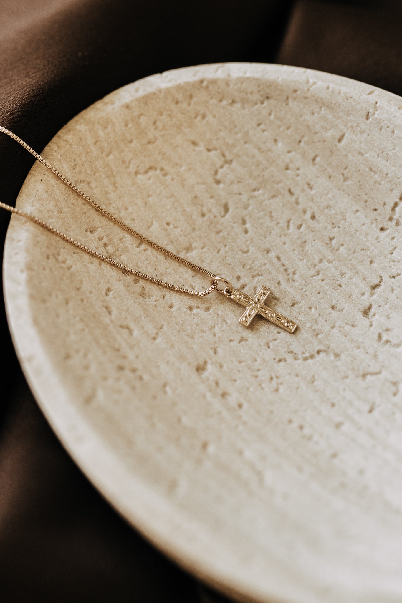 Everyday gold cross pendant necklace photographed on cream stone dish
