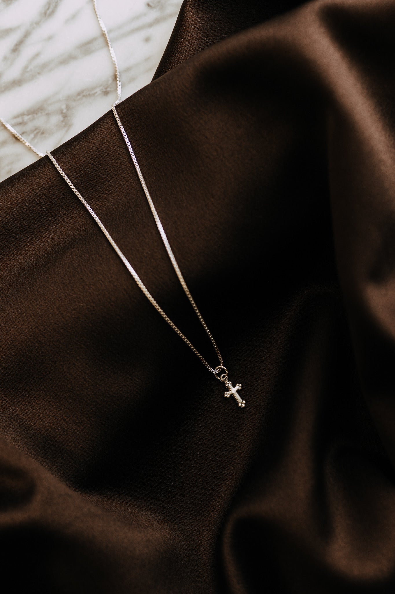 Delicate silver cross pendant photographed on dark satin fabric