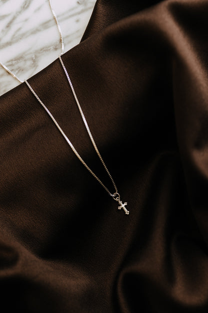 Delicate silver cross pendant photographed on dark satin fabric