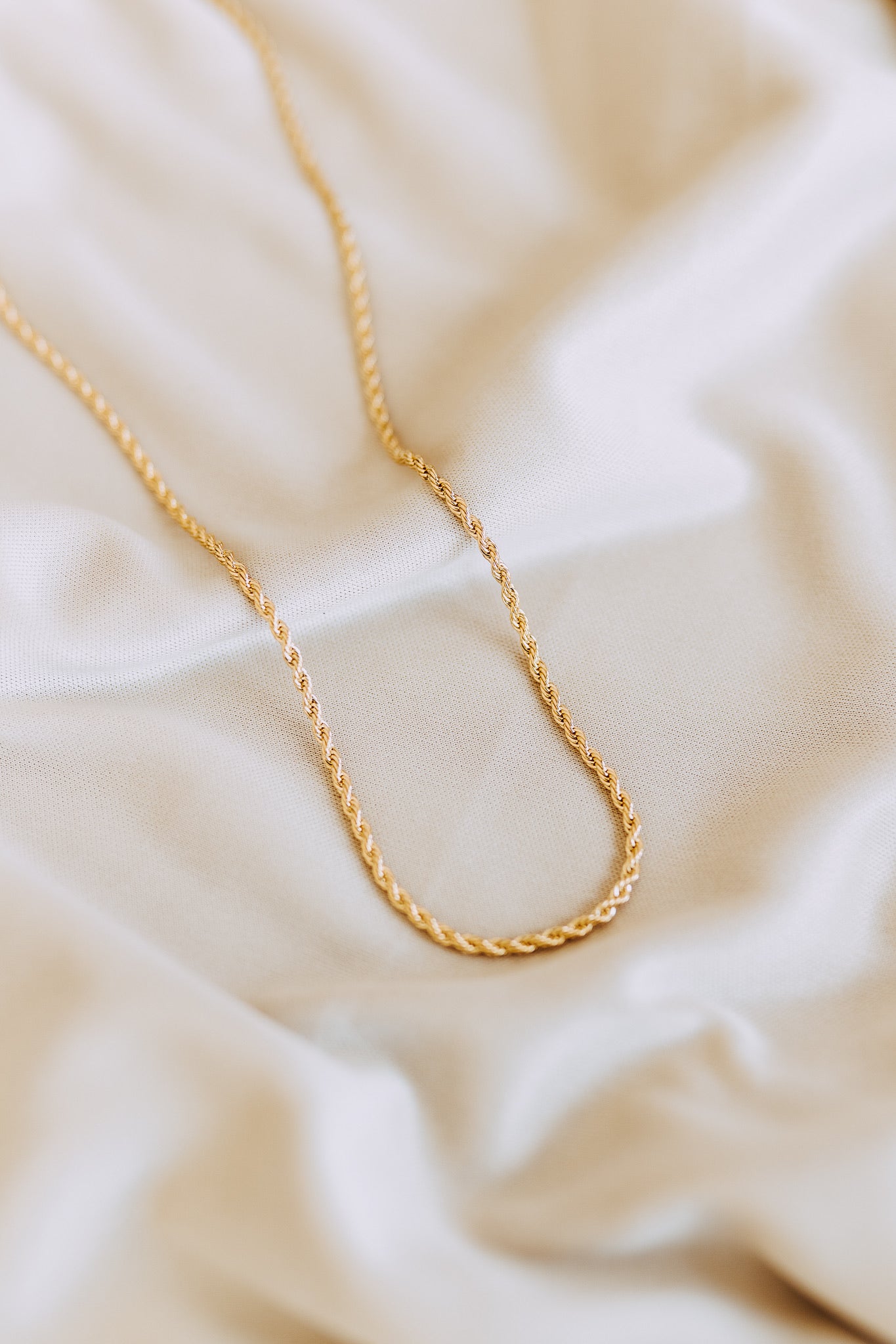 Flat lay of men’s 2mm gold rope chain necklace on soft white fabric background