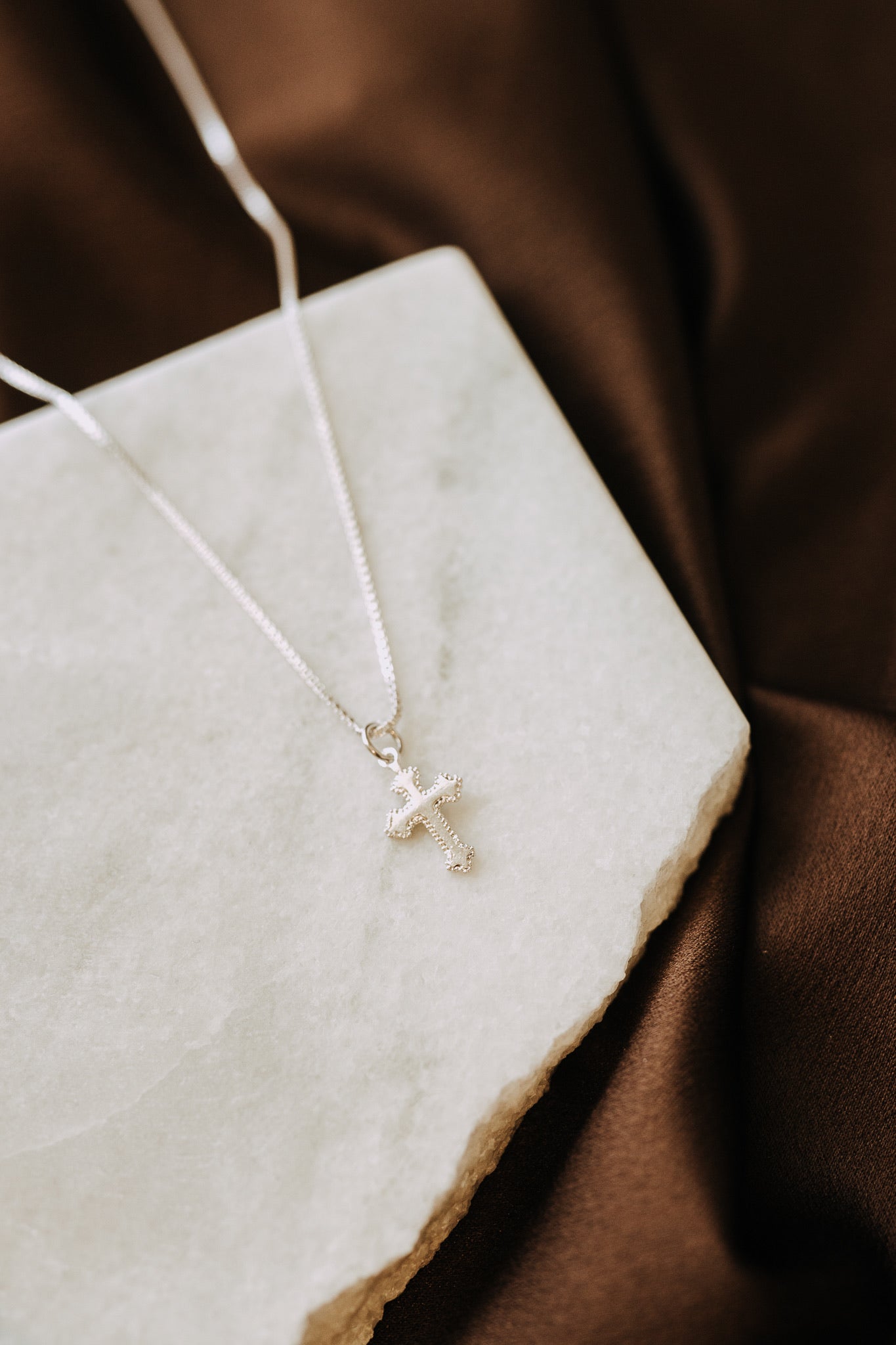 Everyday sterling silver cross necklace photographed on stone tray