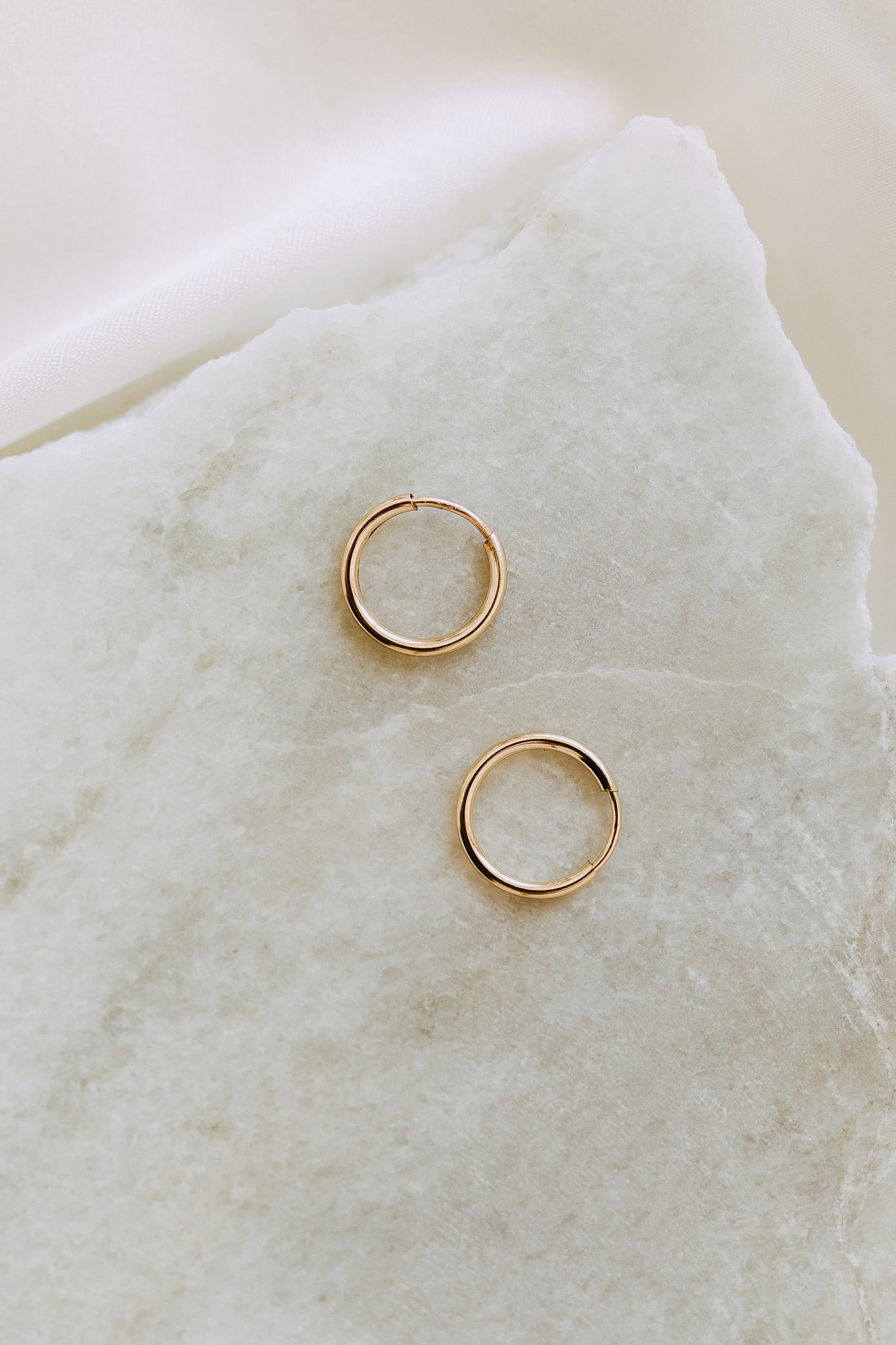 Pair of gold sleeper hoop earrings displayed on white marble stone