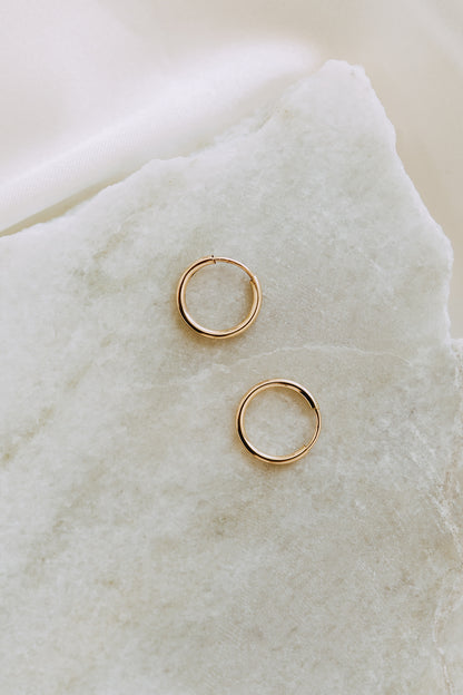 Pair of gold sleeper hoop earrings displayed on white marble stone